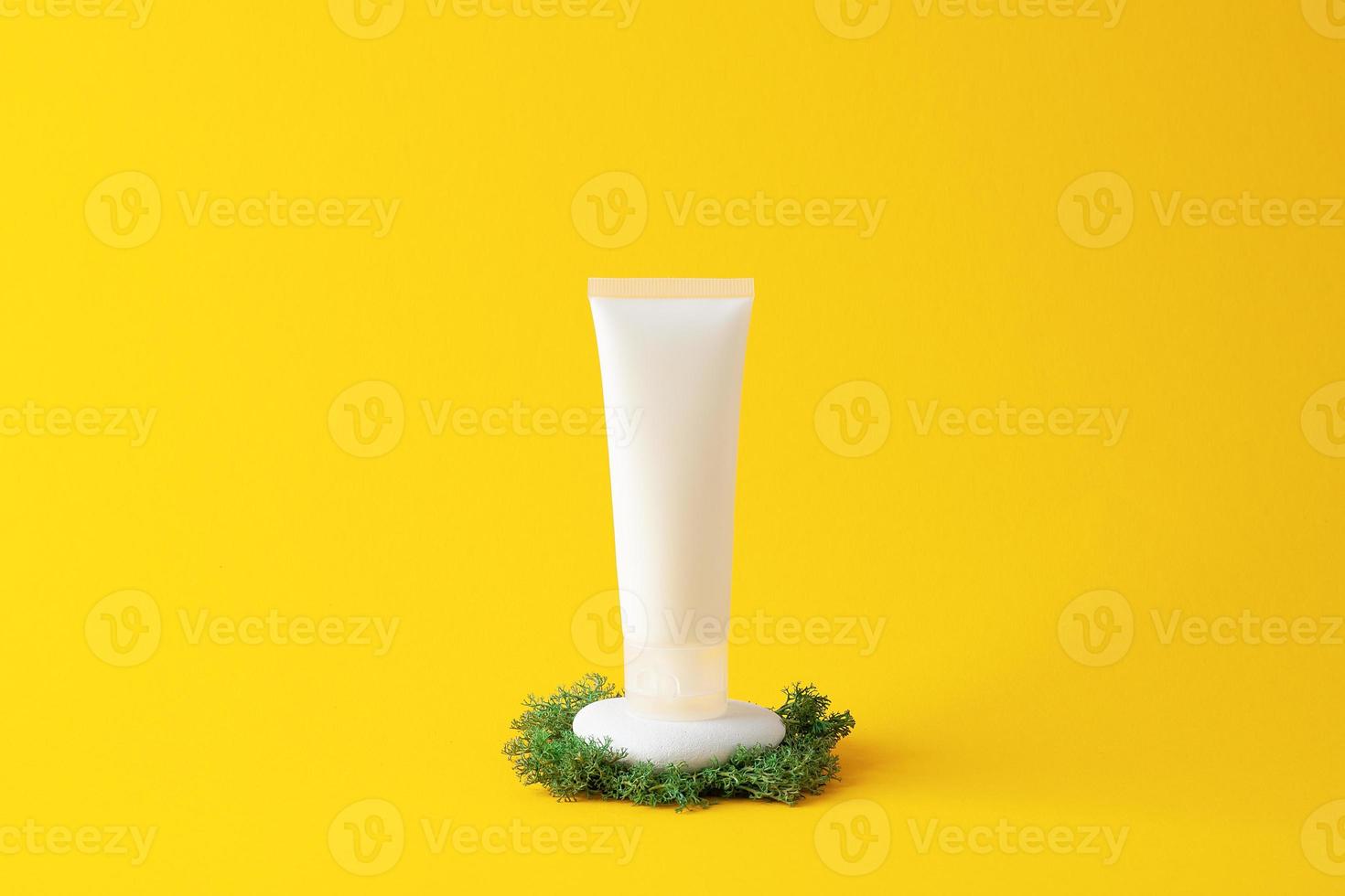 White tube of cosmetic cream on a stone podium with moss on yellow background. Close up. photo