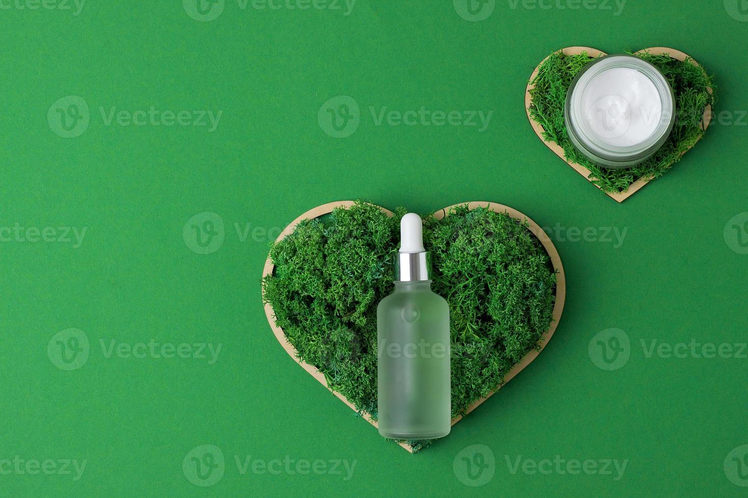 Cosmetic skin care products with a wooden heart and moss on green background. Flat lay, copy space photo