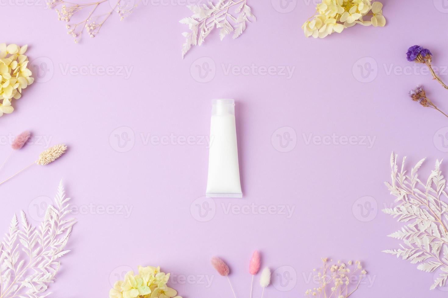 White tube of cosmetic cream with flowers on rose background. Flat lay photo