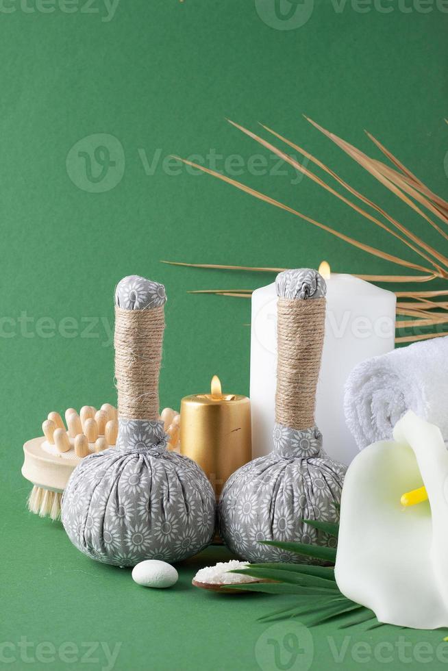 Spa treatment with herbal bag, candles and palm leaf on green background. Close up, copy space photo