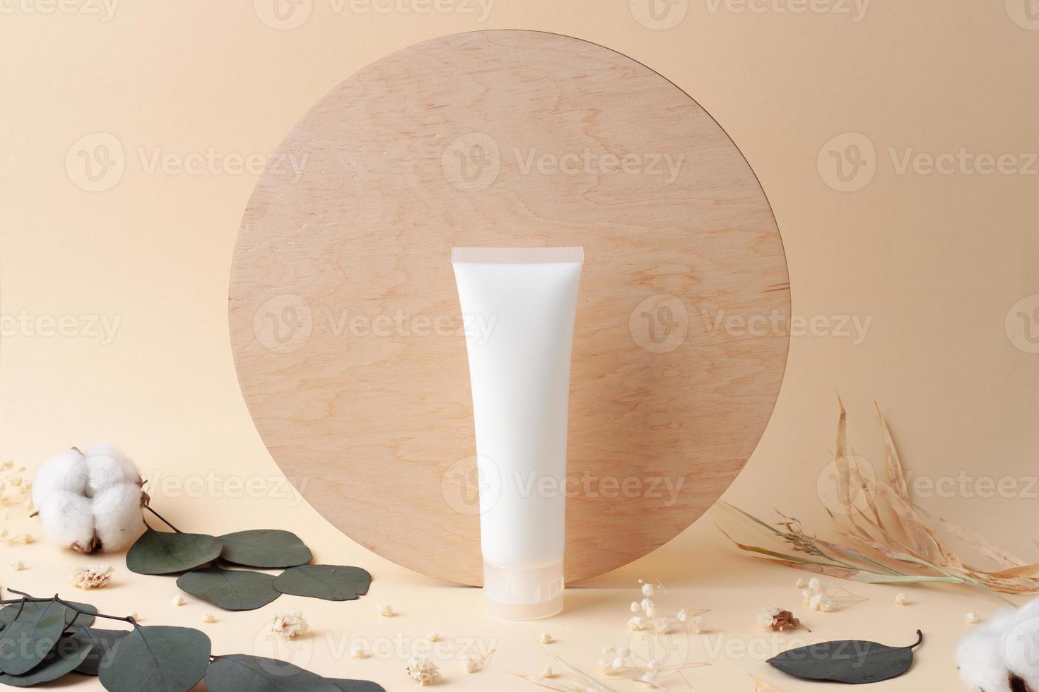 White tube of cosmetic cream with flowers on beige background. Close up. photo