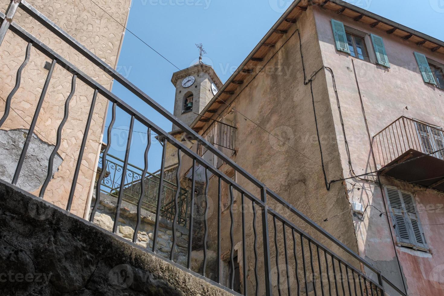 Stone tower with clock and bell, up view to the bell tower, ancient church with a watch, a small village in the mountains in France, European stone chapel in the townlet, old Europe town architecture. photo