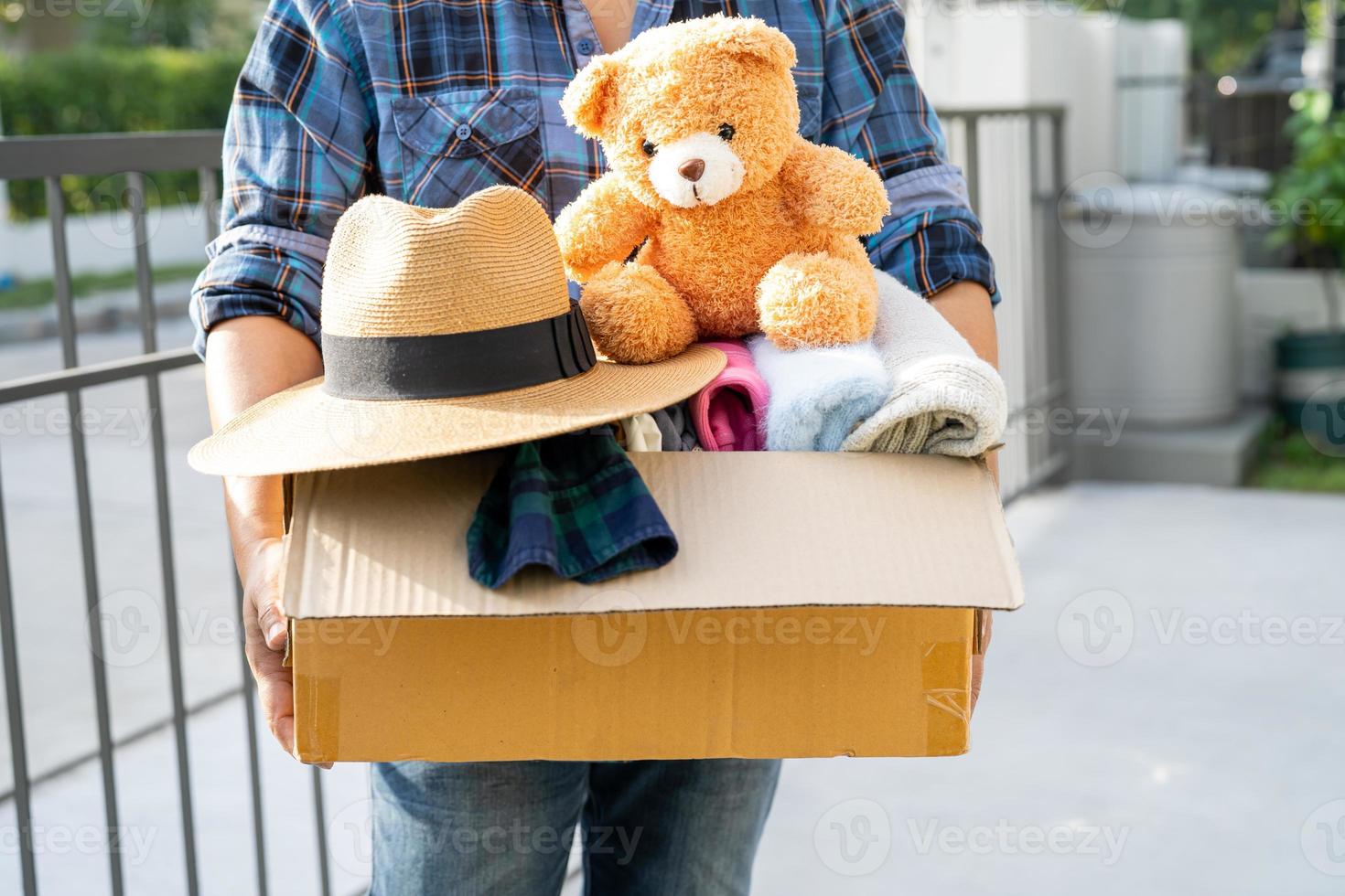 Holding clothing donation box with used clothes and doll at home to support help for poor people in the world. photo