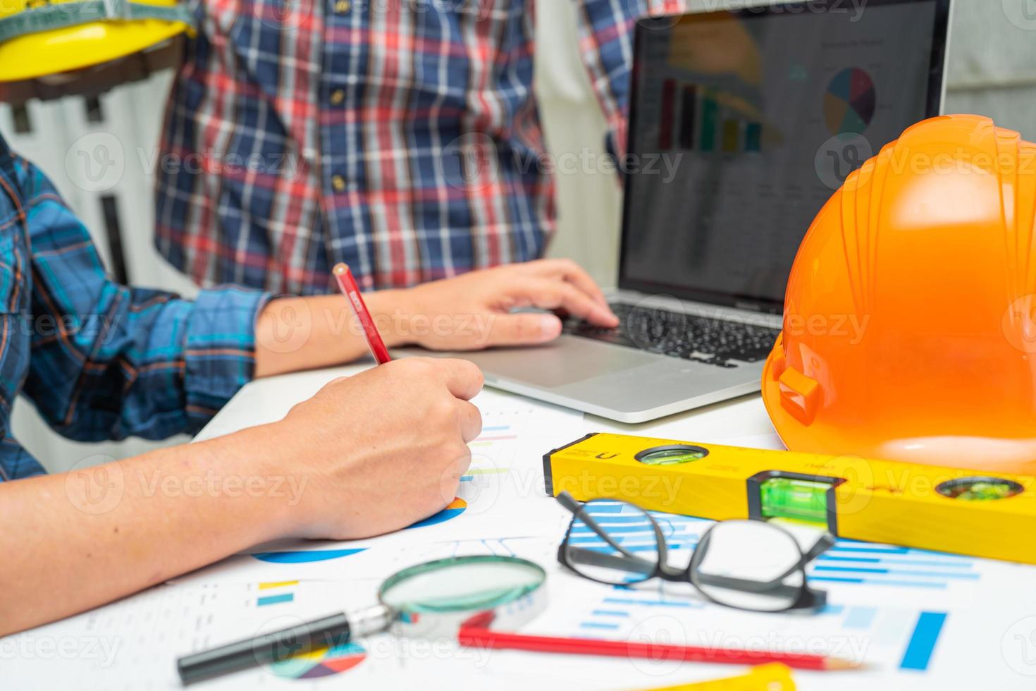 Asian engineer and partner team learn and talk with house plan project blueprint, graph and yellow helmet and engineering construction tools on table work. photo