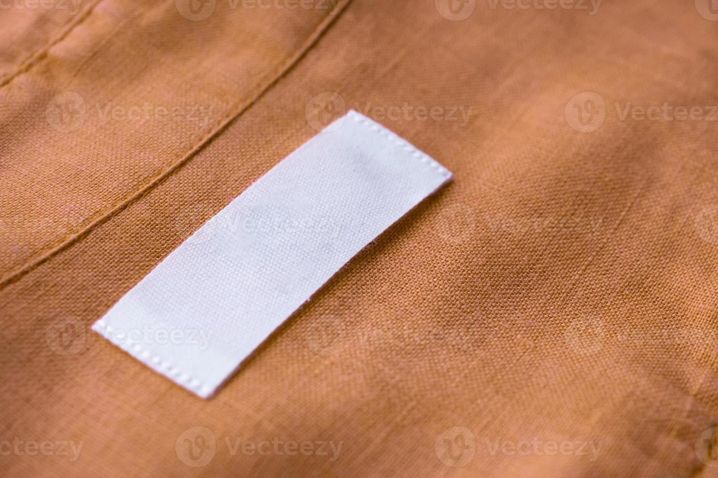 White blank clothing tag label on brown linen shirt fabric texture background photo