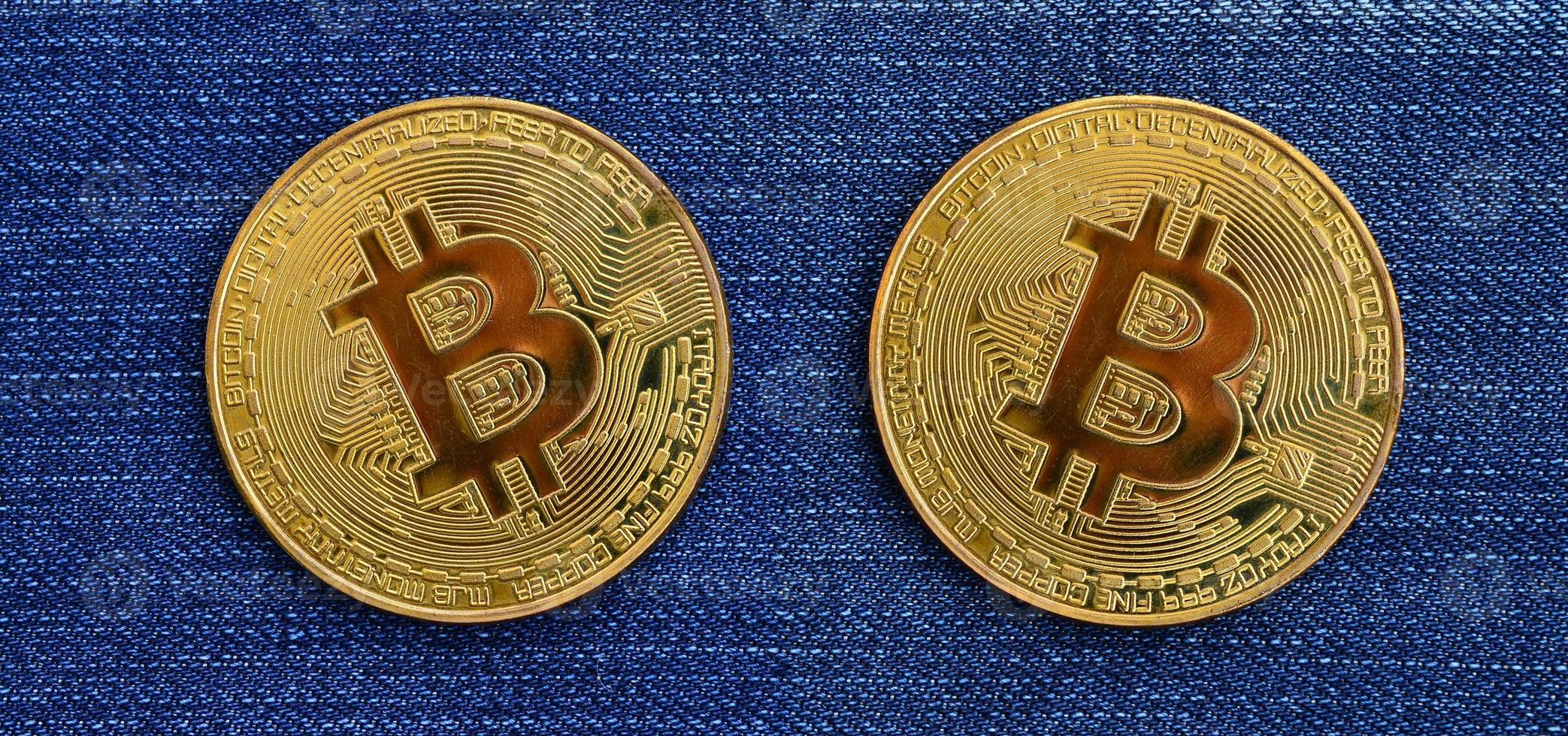 Two golden Bitcoins is lies on a blue jeans fabric. New virtual money. New crypto currency in the form of the coins photo