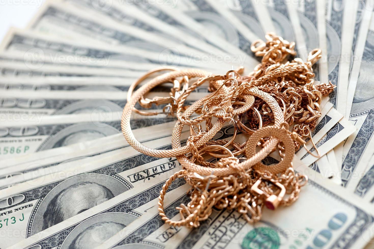 Many expensive golden jewerly rings, earrings and necklaces on big amount of US dollar bills close up. Pawnshop or jewerly shop photo