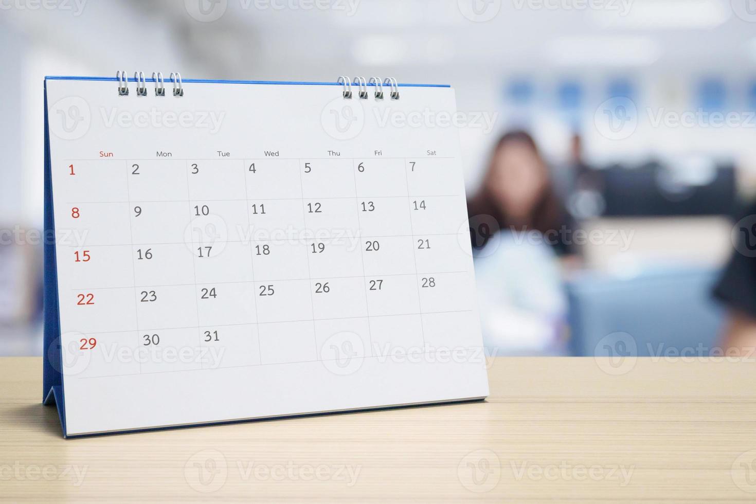 White paper desk calendar on wood table top with blurred office interior background photo