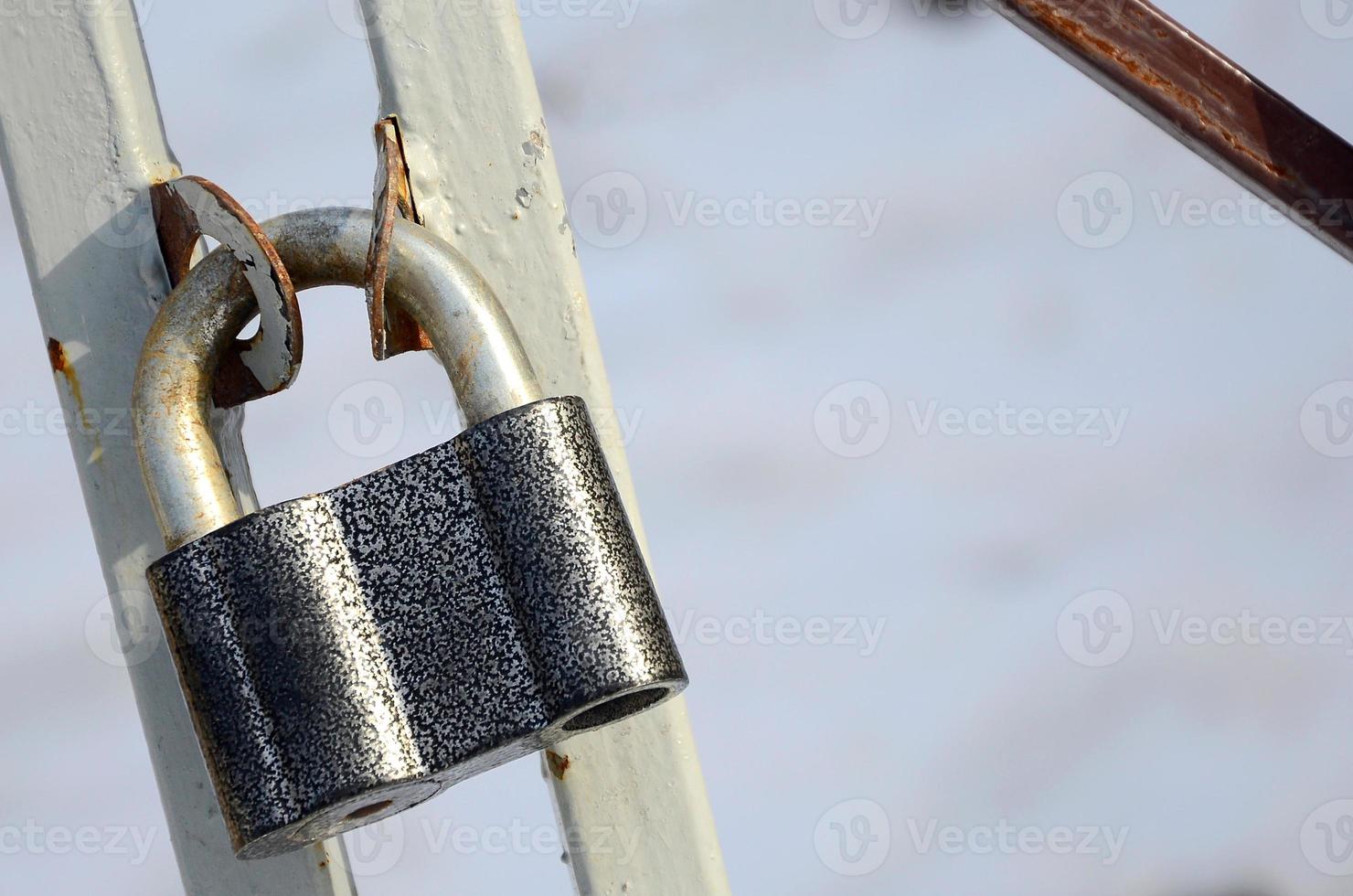 A large gray padlock hangs on a metal gate photo