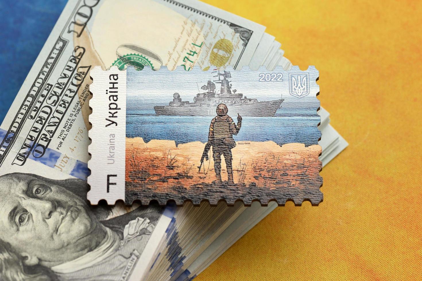 TERNOPIL, UKRAINE - SEPTEMBER 2, 2022 Famous Ukrainian postmark with russian warship and ukrainian soldier as wooden souvenir on big amount of US dollar bills photo