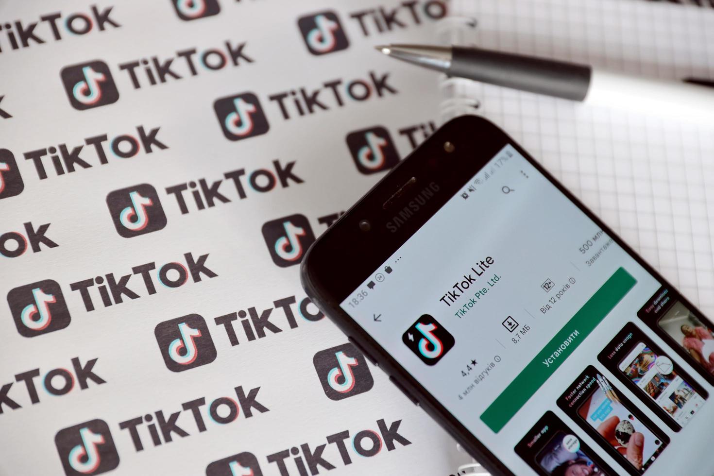 TERNOPIL, UKRAINE - MAY 2, 2022 Tik Tok smartphone app on screen and Many TikTok logo printed on paper. Tiktok or Douyin is a famous Chinese short-form video hosting service owned by ByteDance photo