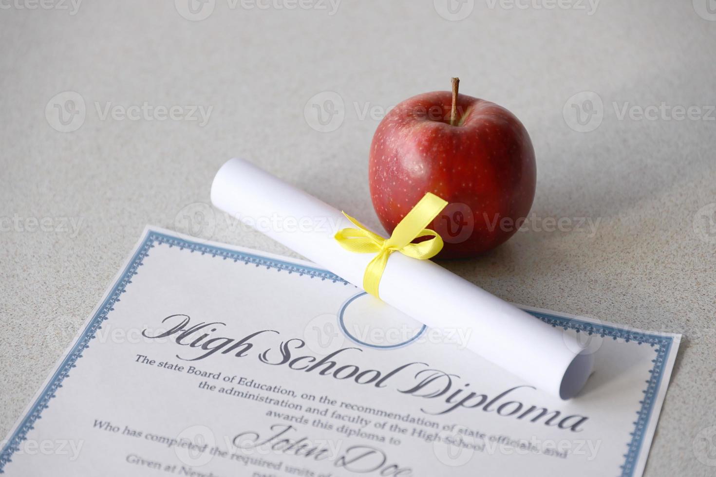 A high school diploma lies on table with small scroll and red apple. Education documents photo