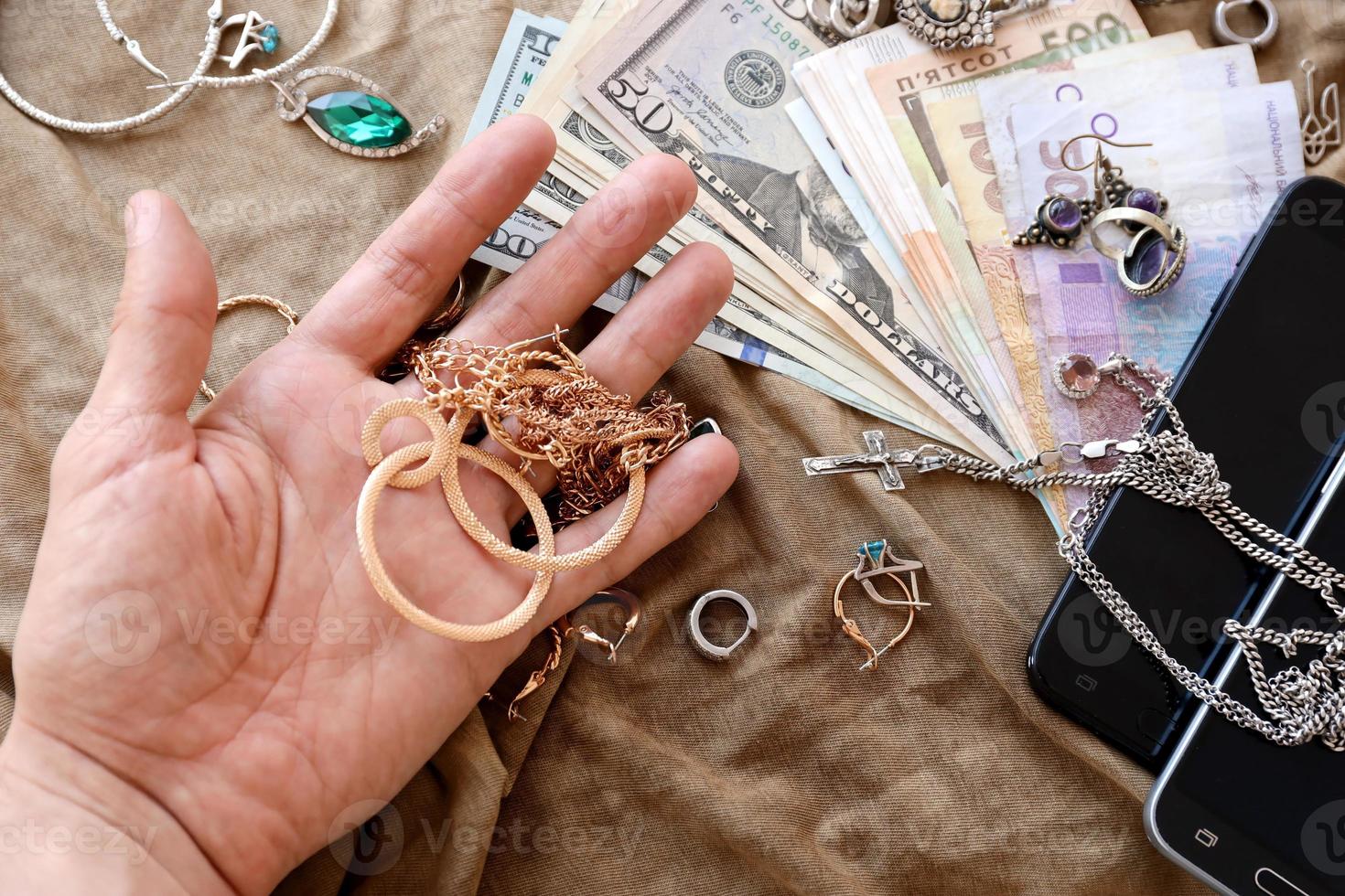 Marauders hand with bunch of stolen jewelry, money and smartphones on military uniform cloth fabric. Looting by Russian soldiers in the Ukrainian cities during Russian invasion on Ukraine photo