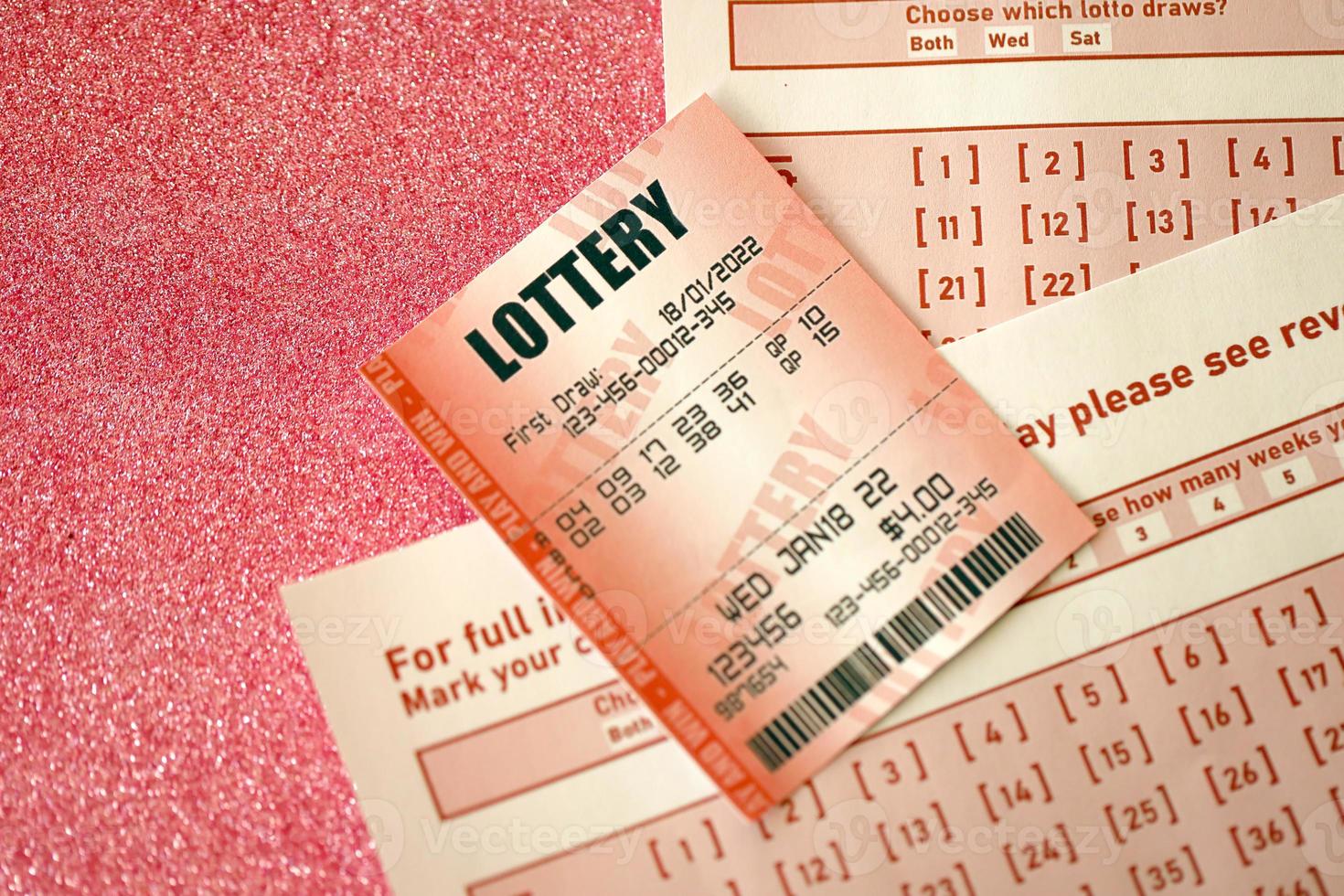 Red lottery ticket lies on pink gambling sheets with numbers for marking to play lottery. Lottery playing concept or gambling addiction. Close up photo