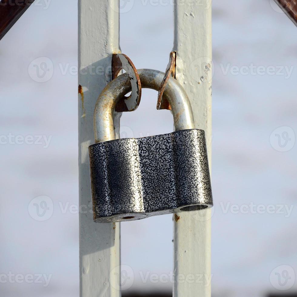 A large gray padlock hangs on a metal gate photo