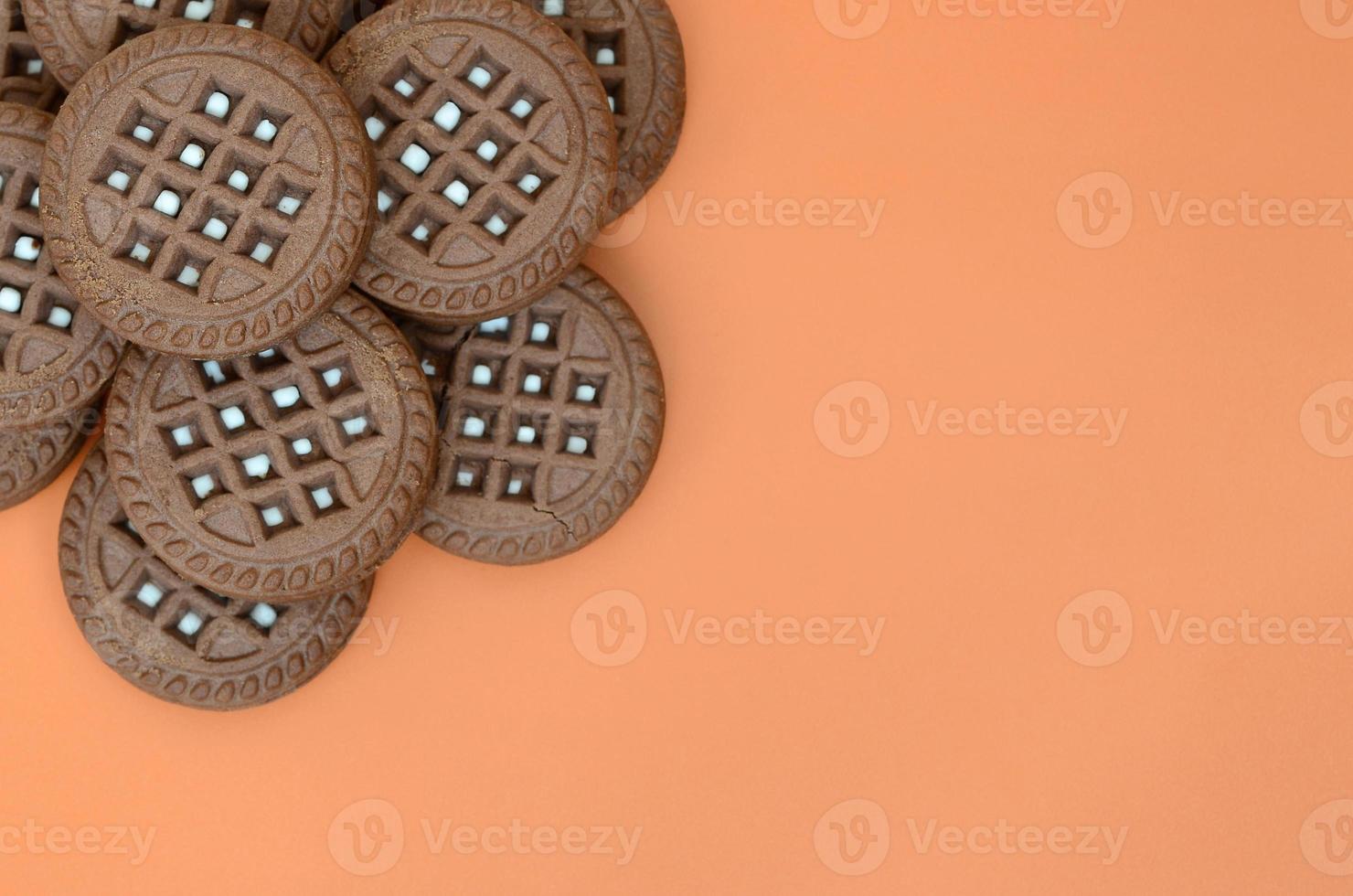 Detailed picture of dark brown round sandwich cookies with coconut filling on an orange surface. Background image of a close-up of several treats for tea photo