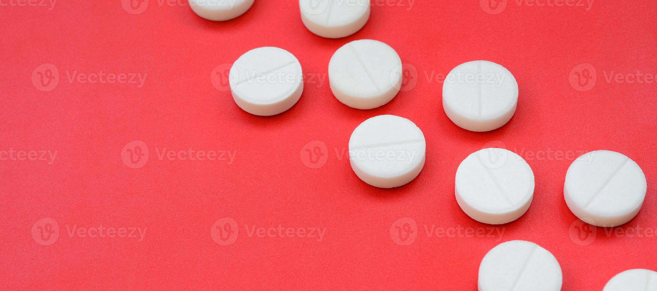 A few white tablets lie on a bright red background surface. Background image on medical and pharmaceutical topics photo