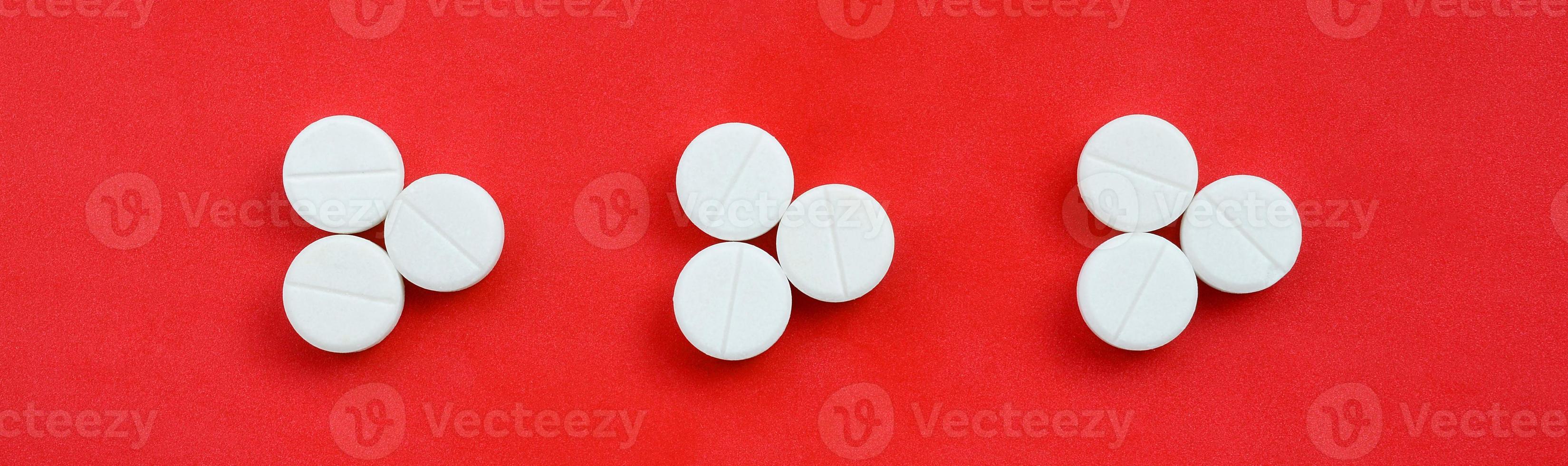 Several white tablets lie on a bright red background in the form of three triangular arrows. Background image on medicine and pharmaceutical topics photo