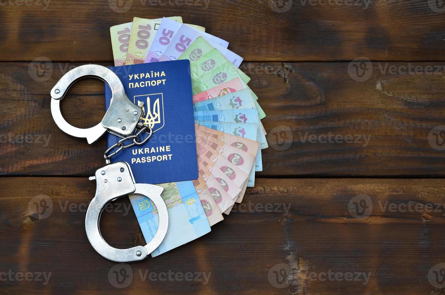 A photograph of a Ukrainian foreign passport, a certain amount of Ukrainian money and police handcuffs. Concept of illegal earnings of Ukrainian citizens abroad photo