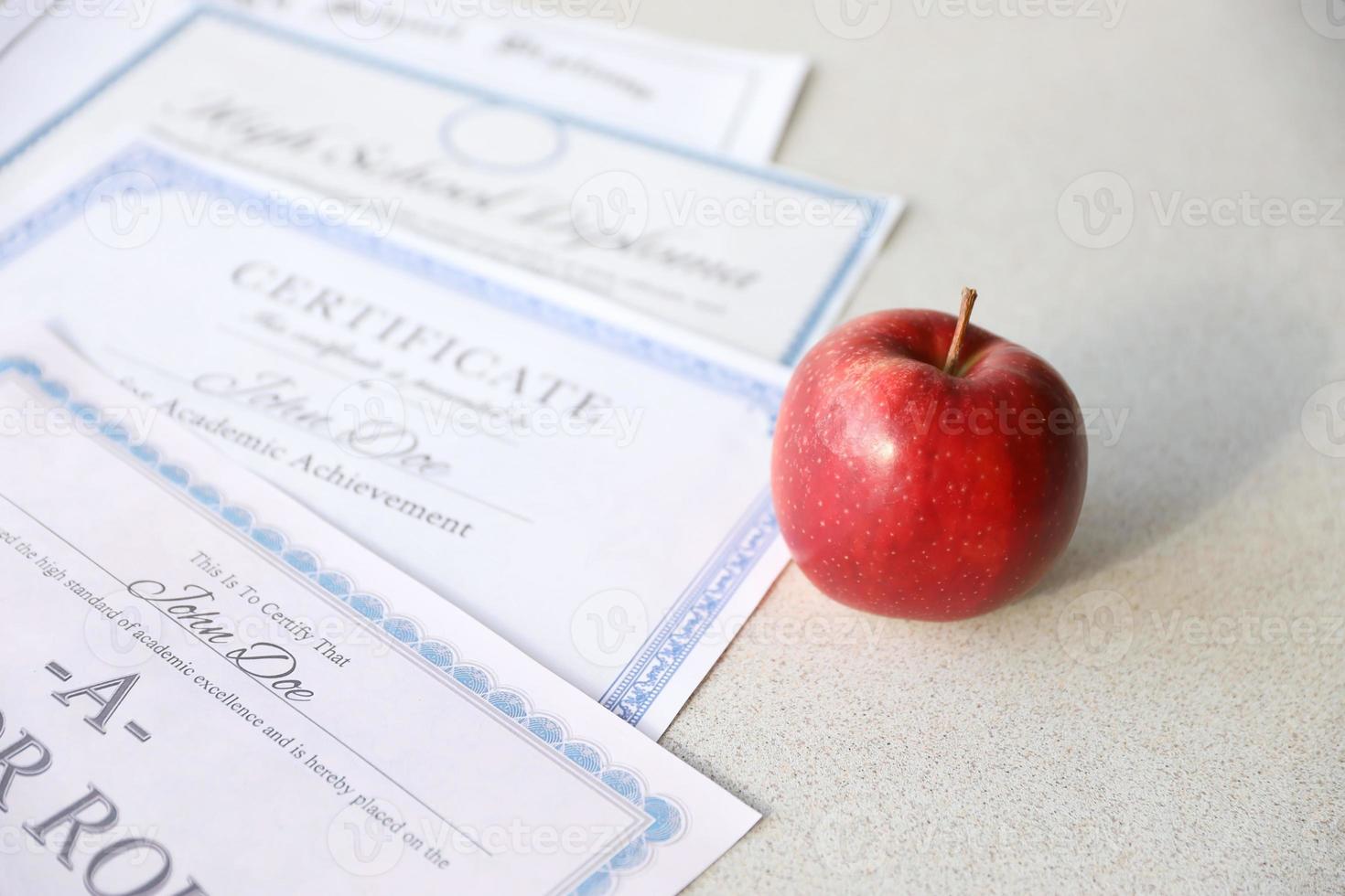 A honor roll recognition, certificate of achievement and high school diploma lies on table with red apple. Education documents photo