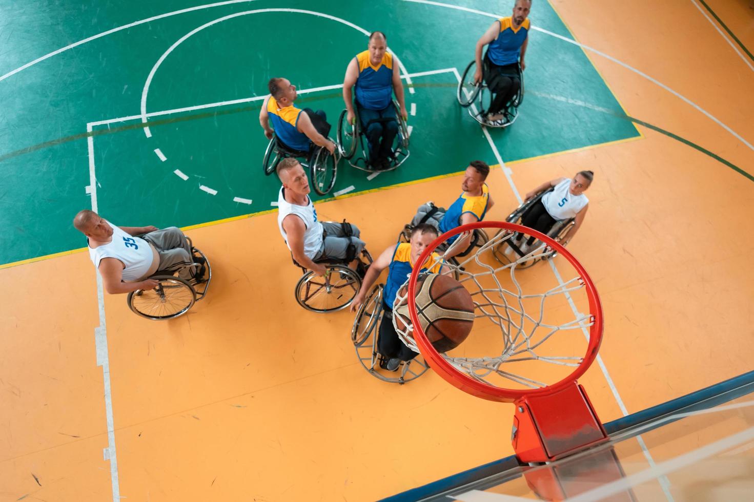 Disabled War or work veterans mixed race and age basketball teams in wheelchairs playing a training match in a sports gym hall. Handicapped people rehabilitation and inclusion concept. photo