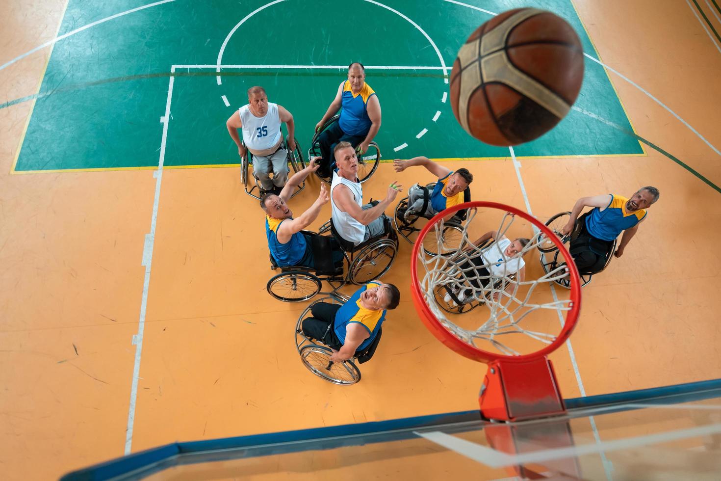 veteranos de guerra o de trabajo discapacitados equipos mixtos de baloncesto de raza y edad en sillas de ruedas jugando un partido de entrenamiento en un gimnasio deportivo. concepto de rehabilitación e inclusión de personas con discapacidad. foto