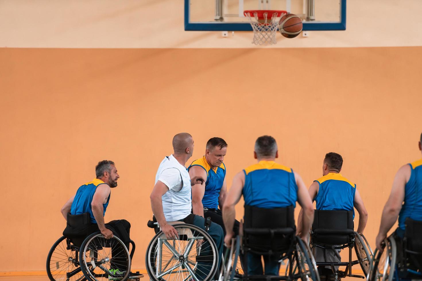 Disabled War veterans mixed race and age basketball teams in wheelchairs playing a training match in a sports gym hall. Handicapped people rehabilitation and inclusion concept photo