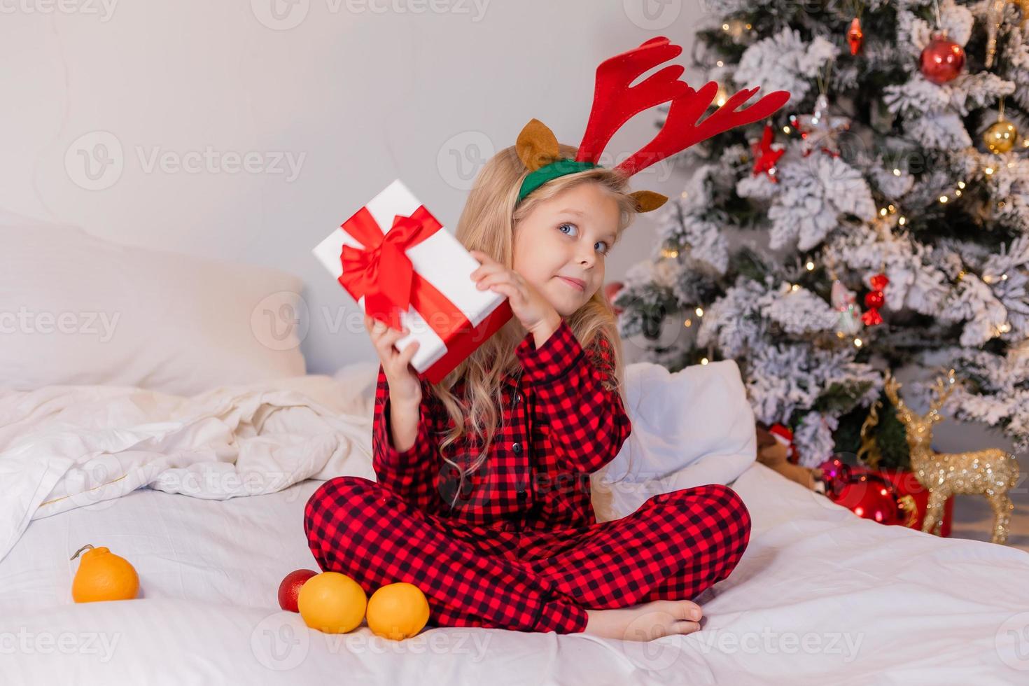 happy little blonde girl at home in pajamas for Christmas sorting presents and playing with Christmas toys photo