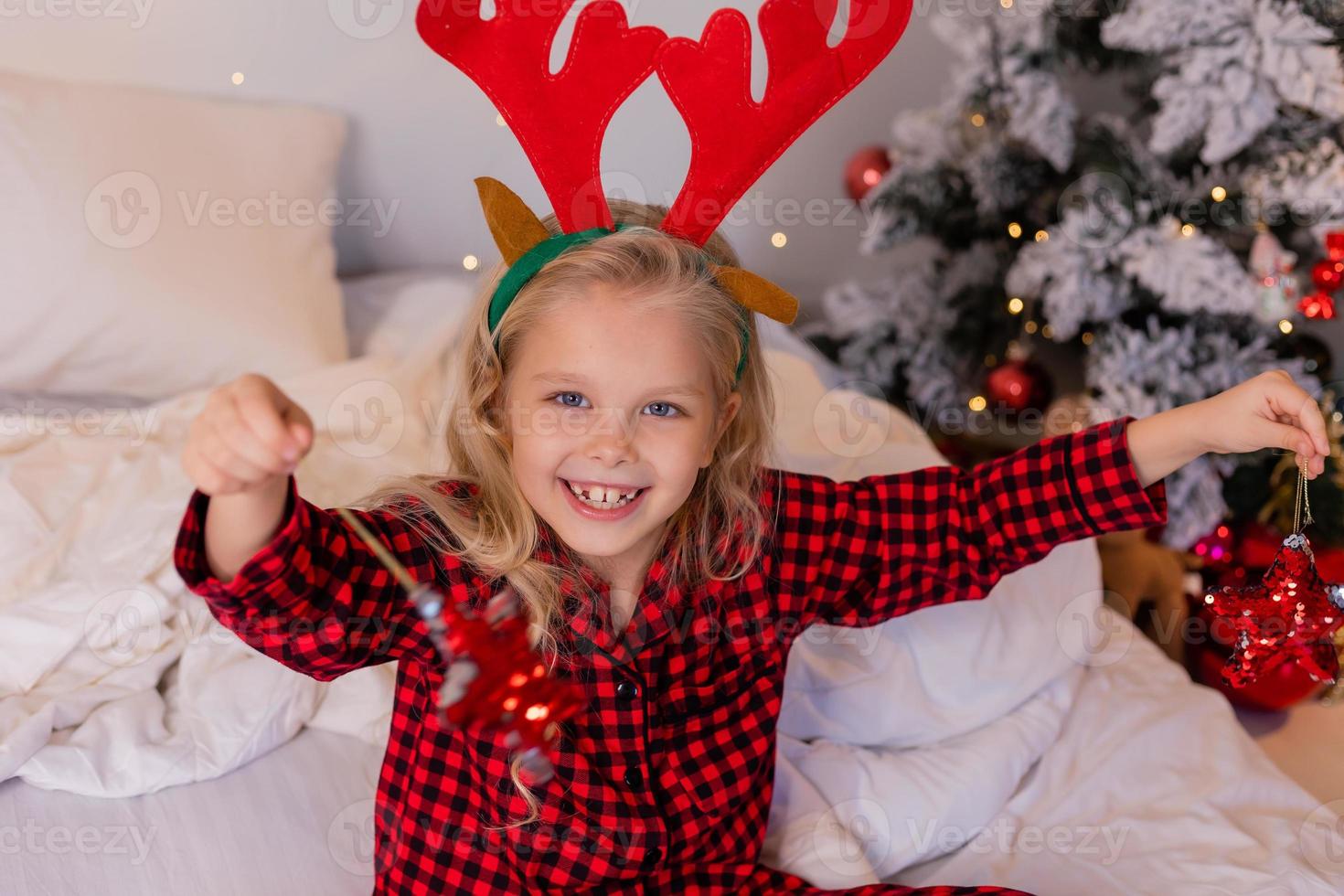 happy little blonde girl at home in pajamas for Christmas sorting presents and playing with Christmas toys photo
