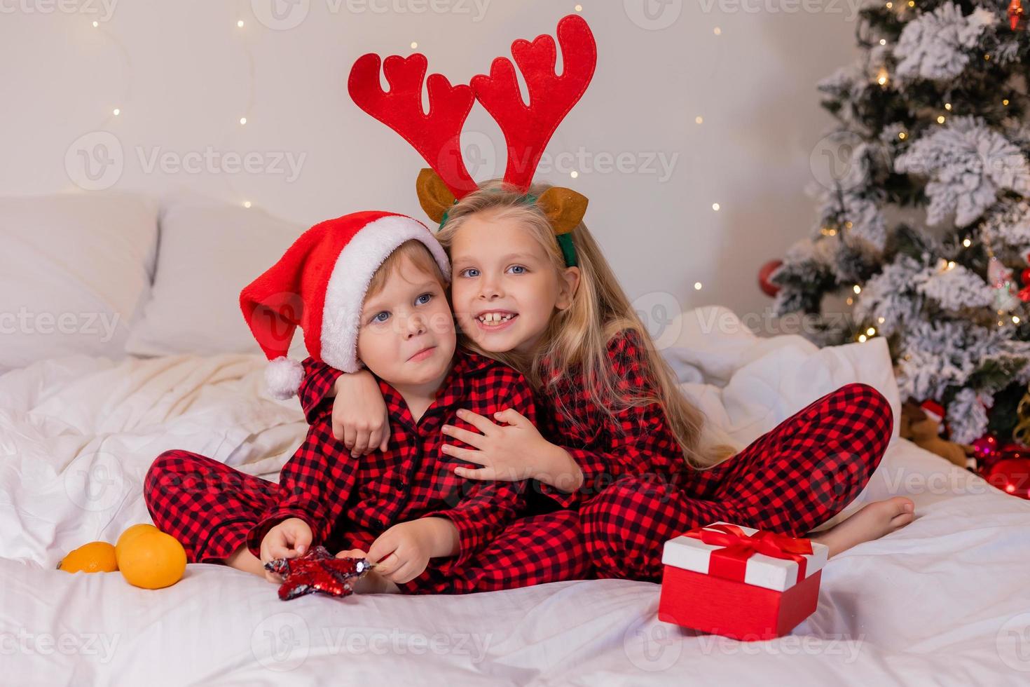 two children at home in pajamas for Christmas are sorting presents and cuddling in bed against the background of a Christmas tree photo
