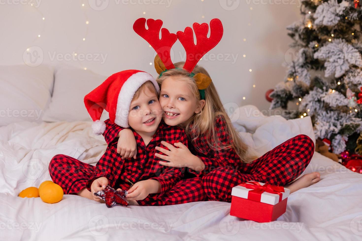two children at home in pajamas for Christmas are sorting presents and cuddling in bed against the background of a Christmas tree photo