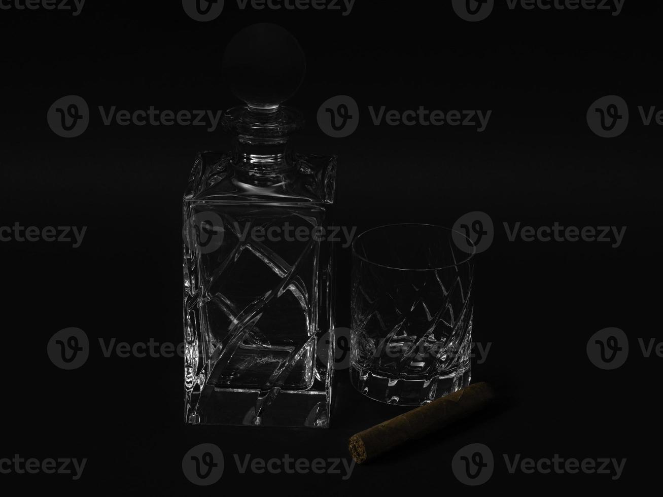 vidrio de cristal y botella de whisky con un cigarro cubano sobre fondo negro foto