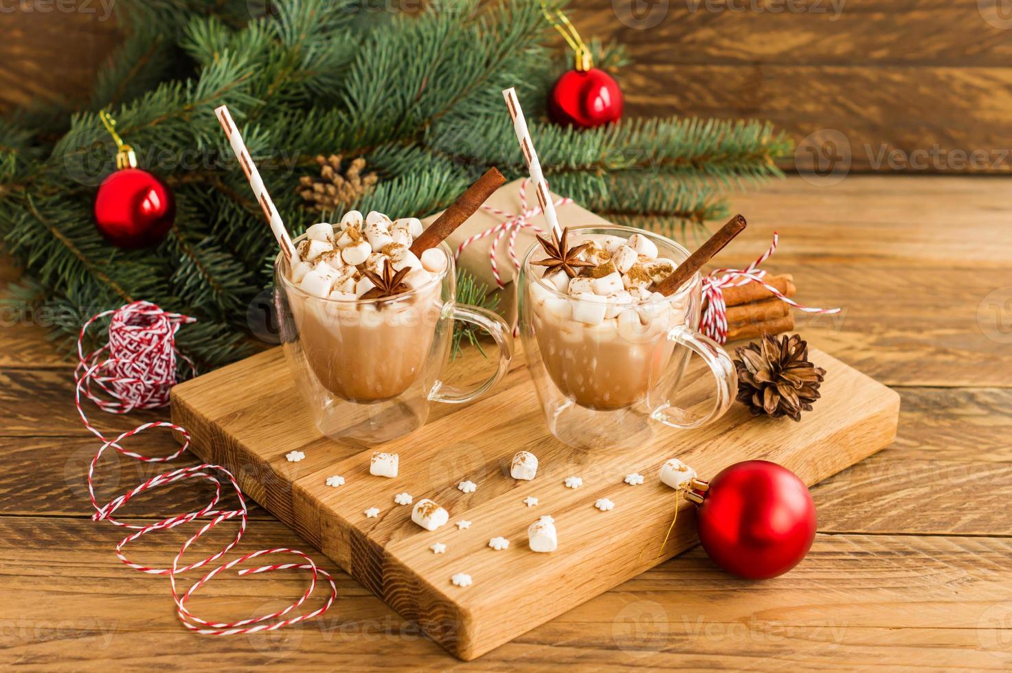New Year's composition of two mugs with hot cocoa and marshmallow on a wooden background with a spruce branch and red balls. photo