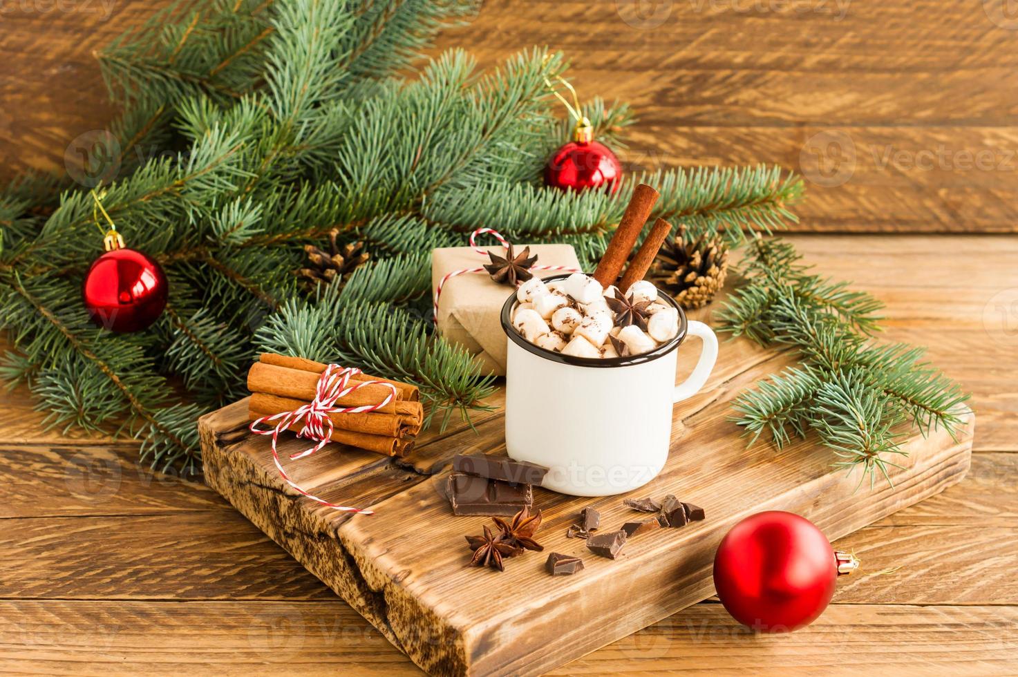 white enameled mug with hot chocolate or cocoa, pieces of chocolate and cinnamon sticks on a wooden board. the concept of a cozy Christmas. photo