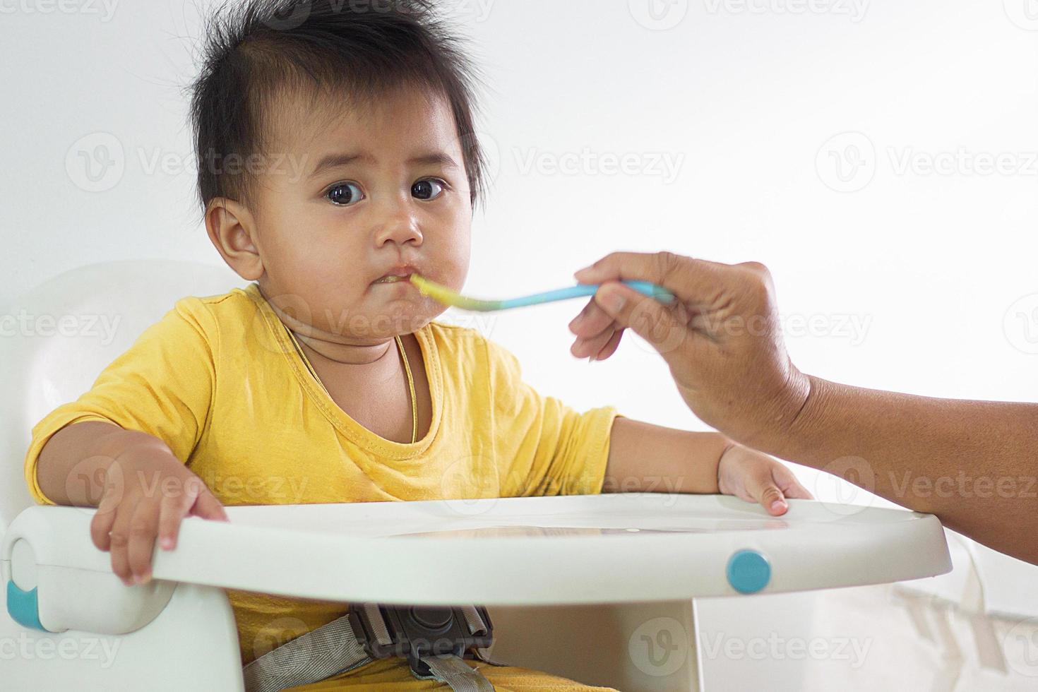 una linda chica blanca sentada en una silla desayunando en el hogar interior alimentando deliciosas comidas que son altamente nutritivas el bebé tiene una cara alegre, divertida, sonriente y feliz en un estilo de vida familiar saludable. foto