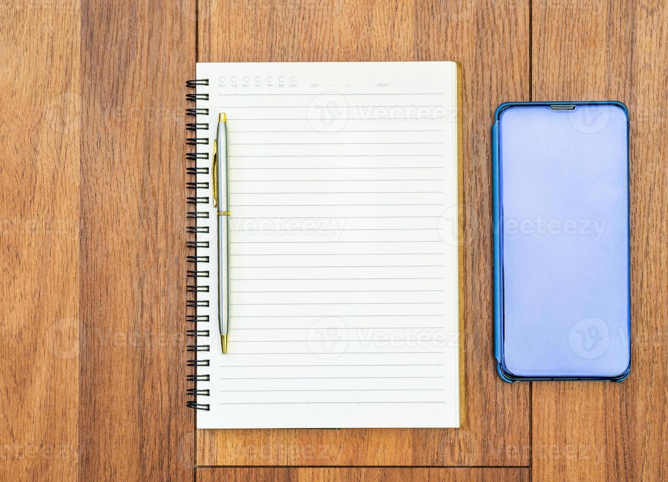 Top view image of open notebook with blank pages and cellphone on wooden table photo