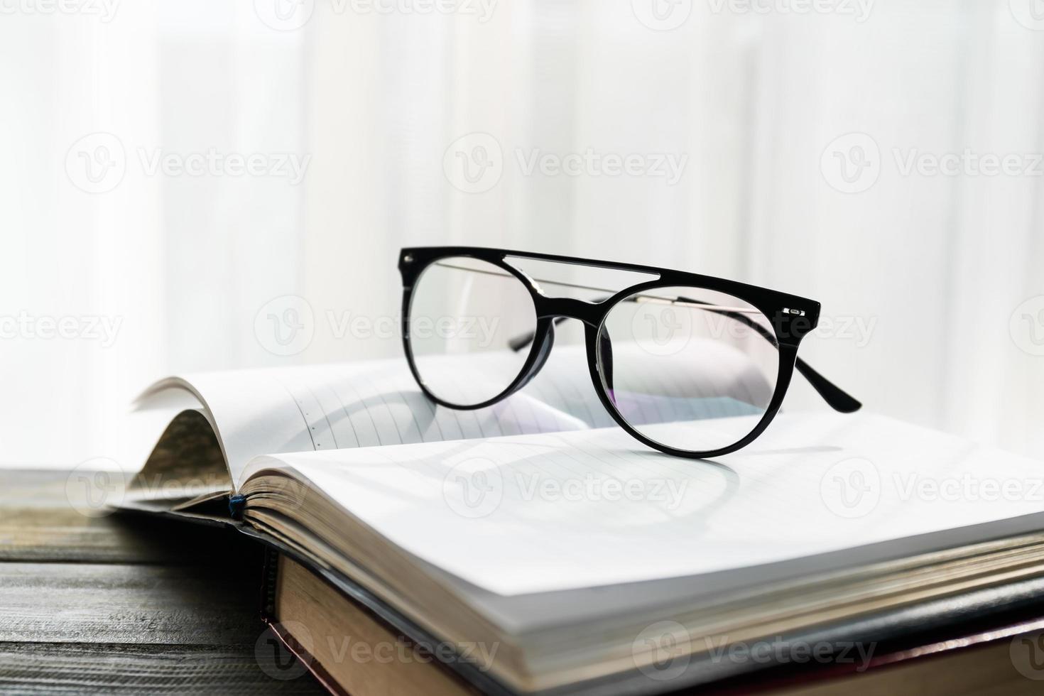 Reading glasses put on open book beside the window photo