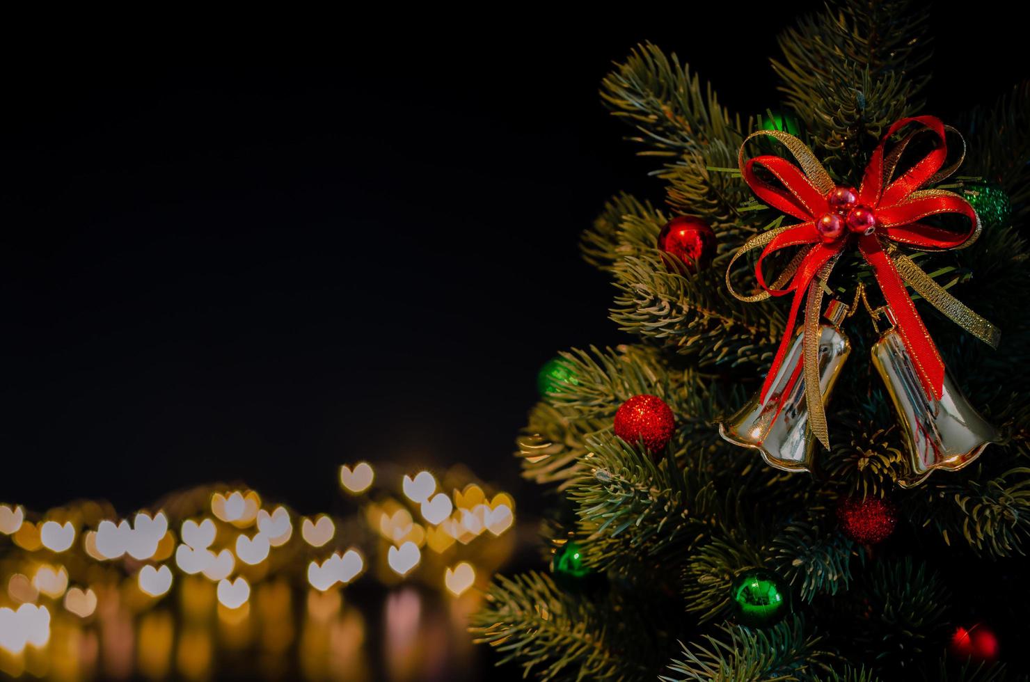 los adornos de campana decoran el árbol de navidad con fondo de luces bokeh en forma de amor. concepto de navidad y año nuevo. foto
