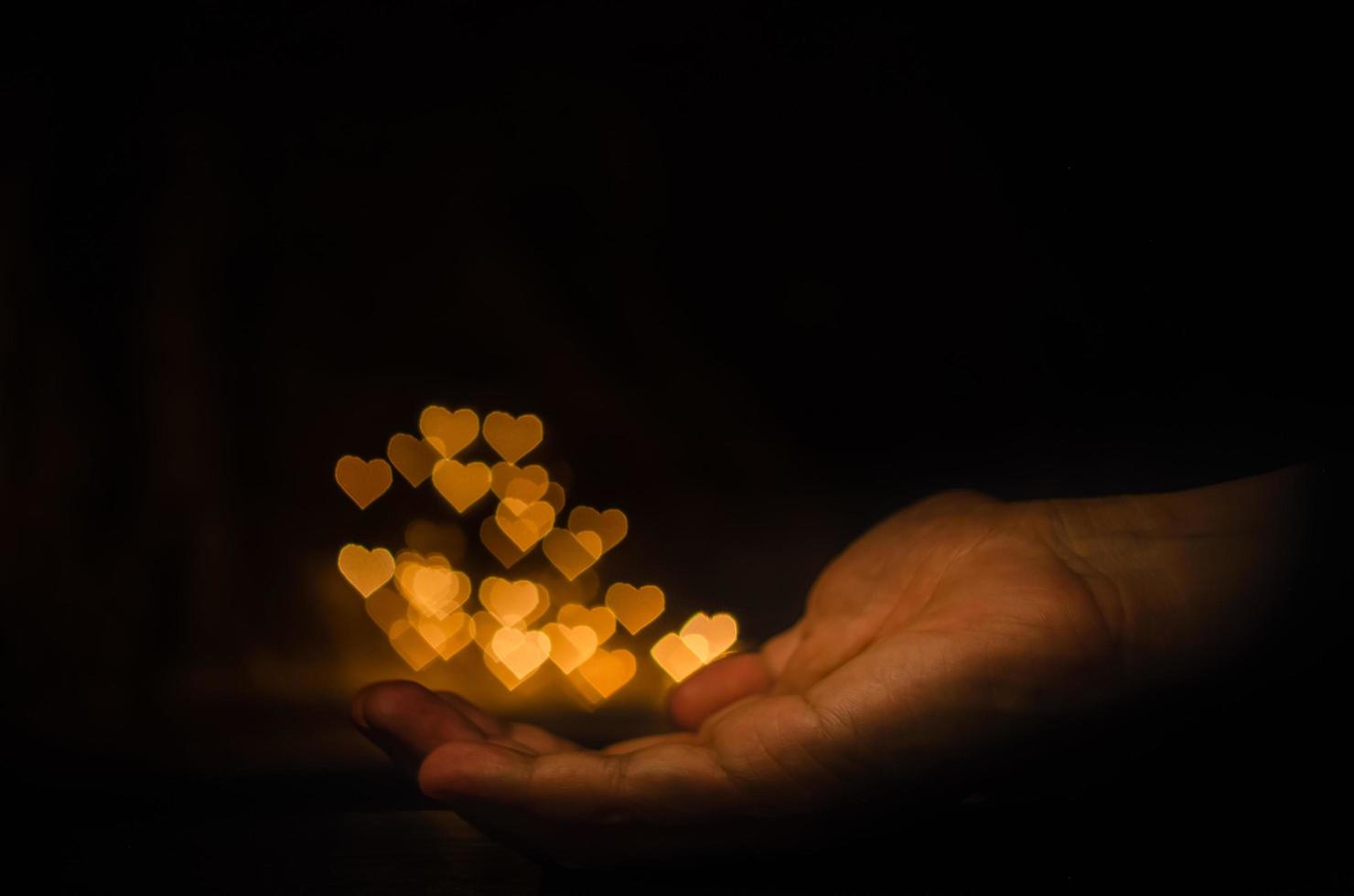 The hand holding yellow love shape bokeh light on black background. photo