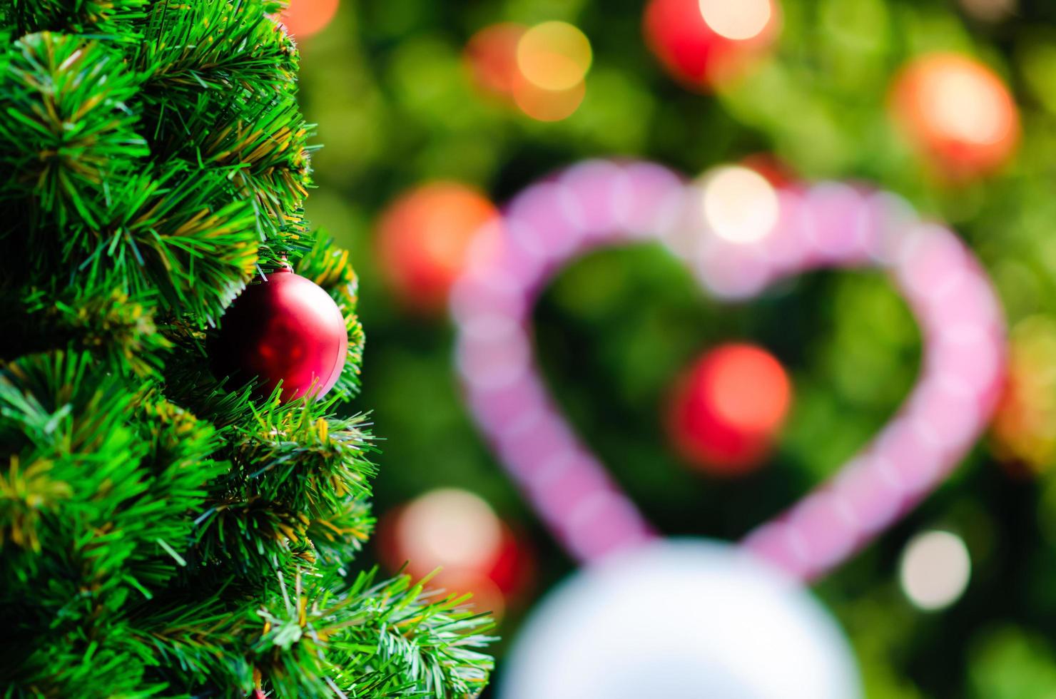 Red bauble hanging on Christmas tree with bokeh background from another bigger Christmas tree. photo