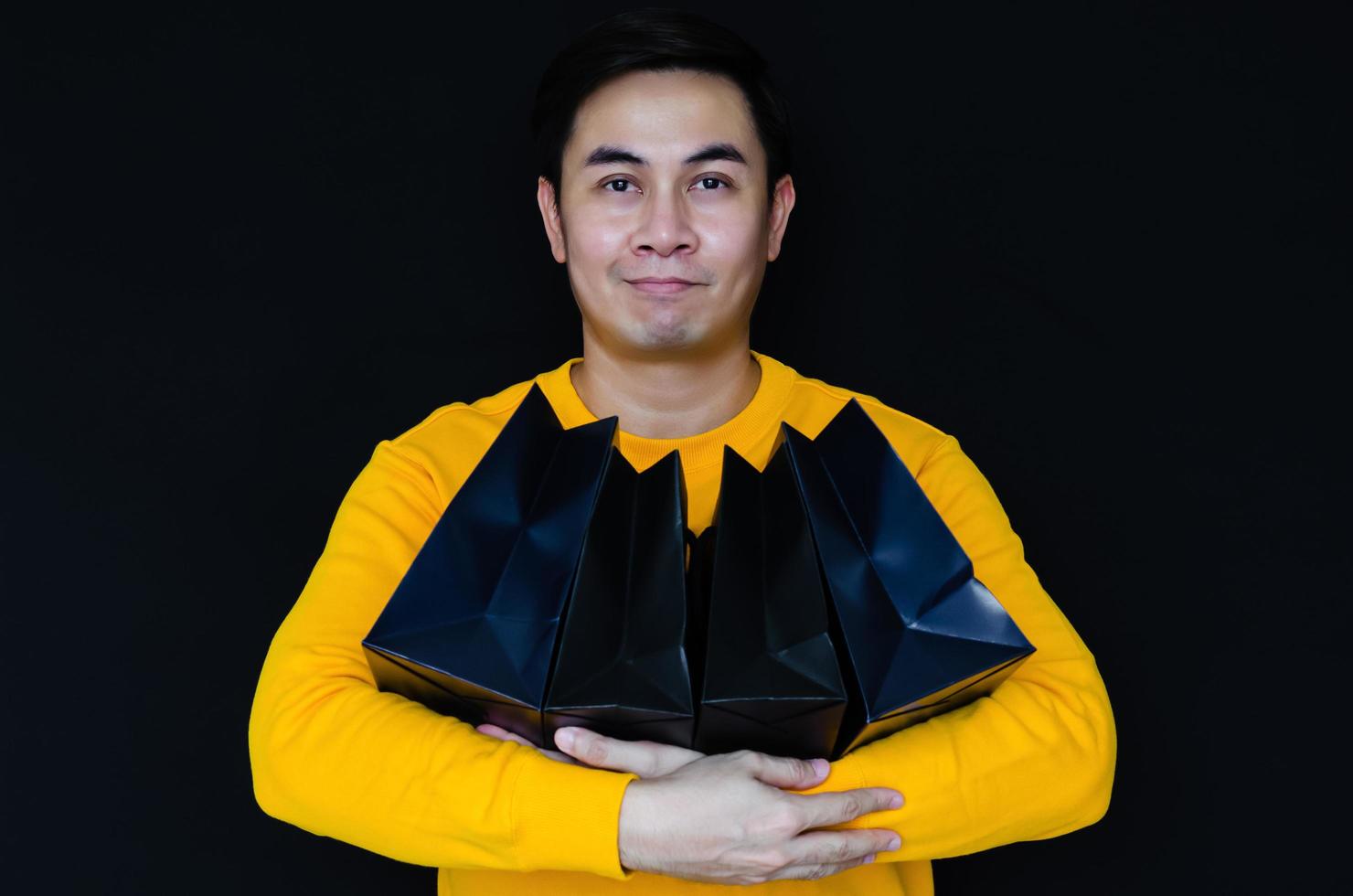 hombre asiático sonriendo y sosteniendo bolsas de compras en un fondo oscuro para el concepto de viernes negro. foto