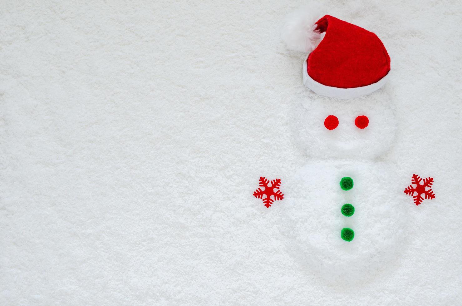 endecha plana de muñeco de nieve con adornos navideños y sombrero de santa claus puesto sobre fondo de nieve. foto