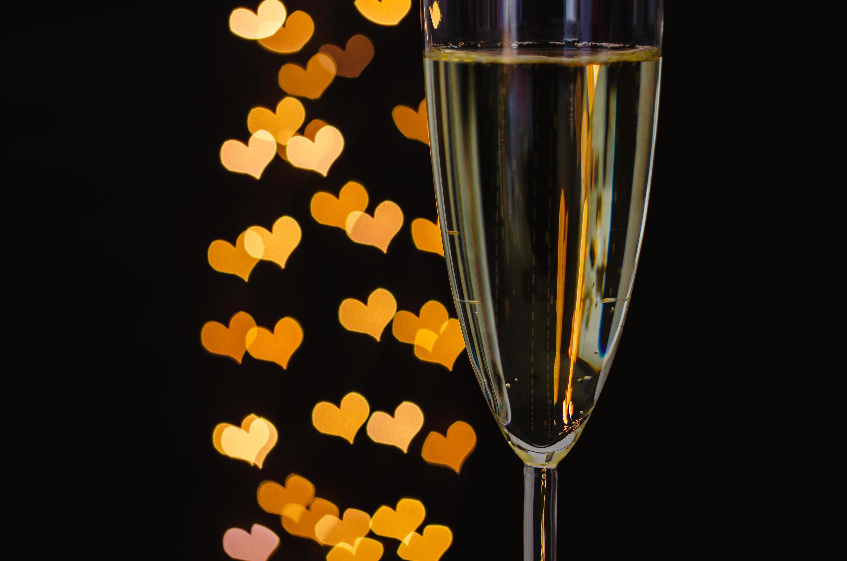 Partial focus of a glass of sparkling wine with golden love shape bokeh