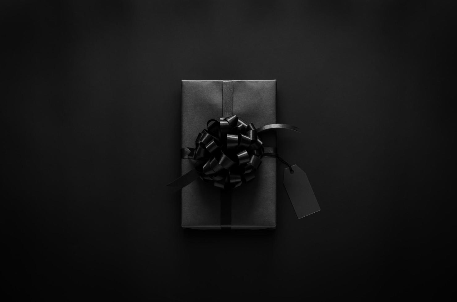 A black gift box with ribbon and blank price tag puts on black background. Black friday and Boxing day concept. photo