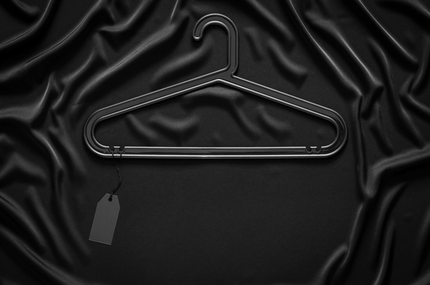 A black hanger with blank black price tag on black smooth and wavy cloth with space for text. Black Friday concept. photo