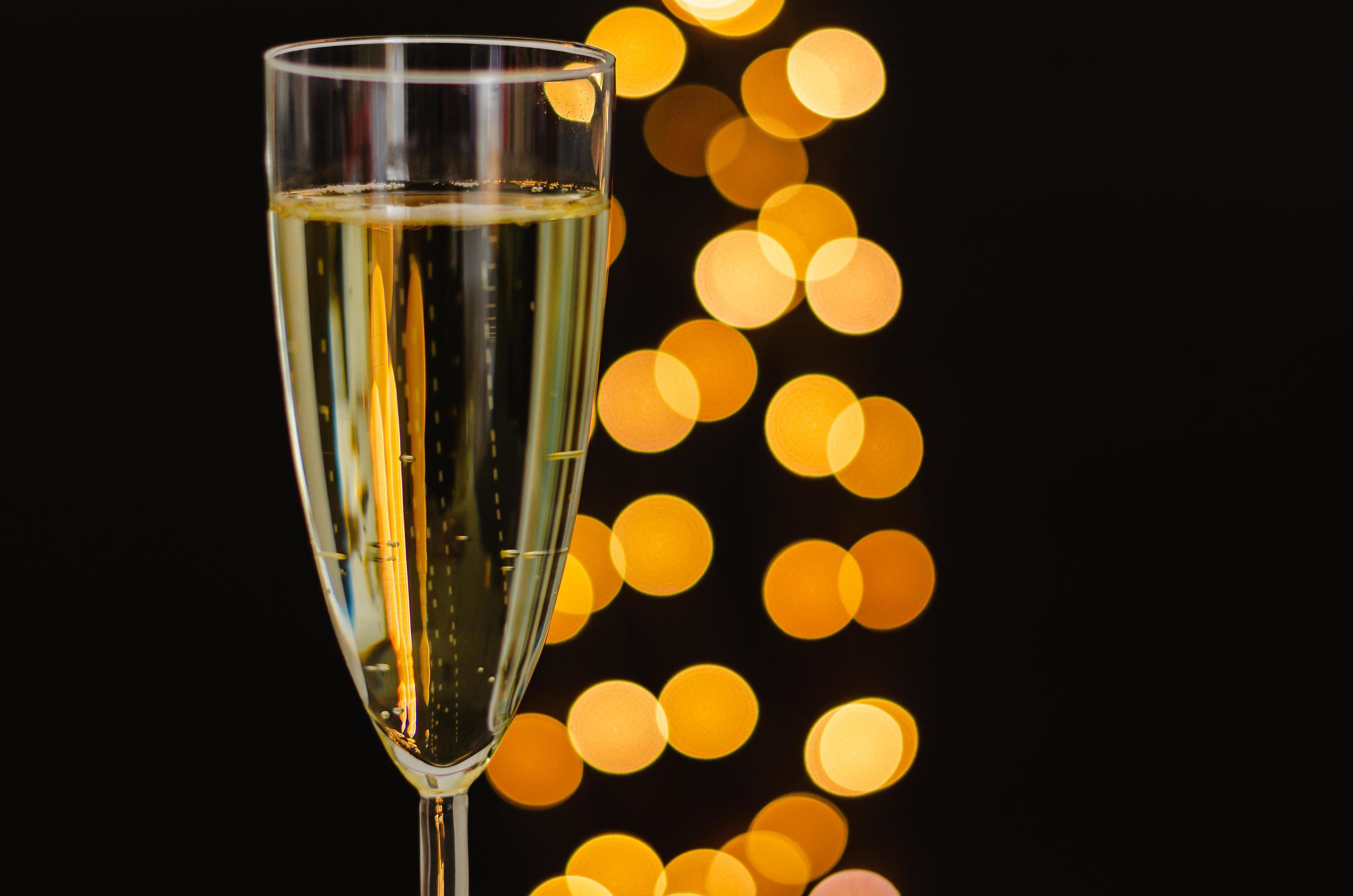 Partial focus of a glass of sparkling wine with golden bokeh lights on