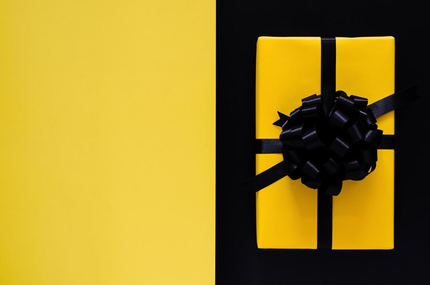 A yellow gift box with black ribbon puts on black and yellow background. Black friday and Boxing day concept. photo