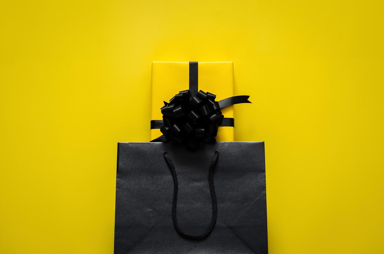 una caja de regalo amarilla se coloca en una bolsa de compras negra con fondo amarillo. concepto de viernes negro y día de boxeo. foto