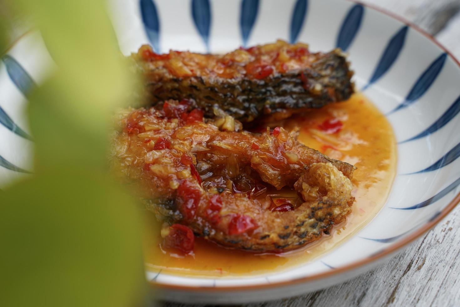 pescado frito con chile en un plato de cerámica sobre un suelo de madera antiguo. el sabor es agrio, dulce y ligeramente picante. foto