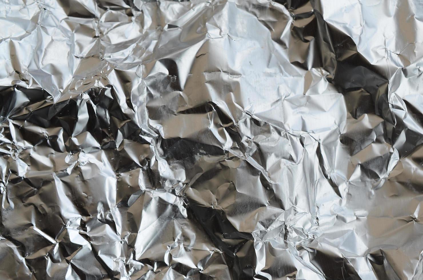 Thin wrinkled sheet of crushed tin aluminum silver foil background with shiny crumpled surface for texture photo